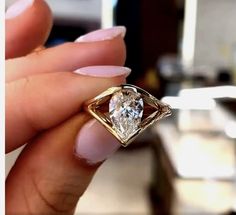 a woman's hand holding an engagement ring with a diamond in the center, on top of her finger