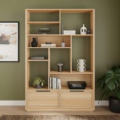 a wooden shelf with books and vases on it in front of a green wall