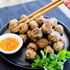 a black plate topped with meatballs and chopsticks next to a bowl of dipping sauce