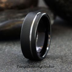 a black and silver wedding band with a thin center is shown in front of some rocks