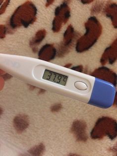 a digital thermometer being held up in front of a leopard print blanket with brown spots on it