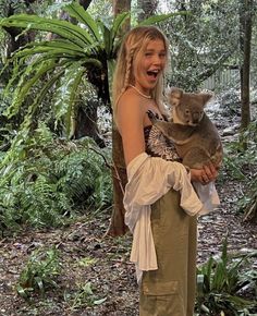 a woman holding a baby koala in her arms while standing next to a tree