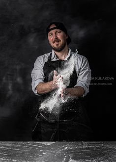 a man in an apron is throwing flour into the air with his hands on a table