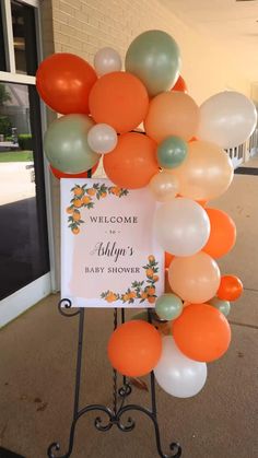 an orange and white welcome sign with balloons in the shape of a wreath on a stand