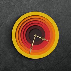 a clock made out of colored paper sitting on top of a black surface with yellow and red circles