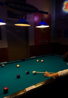 a man playing pool in a dark room with two lamps on either side of the pool table