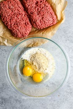 two raw hamburger patties and eggs in a glass bowl on a marble counter top