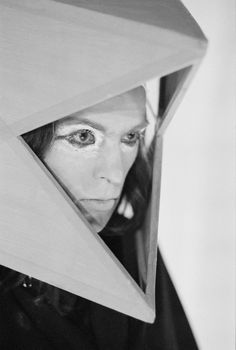 black and white photograph of a woman looking through a triangular shaped object with her eyes wide open