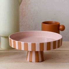 an orange and white striped bowl sitting on top of a wooden table next to a vase