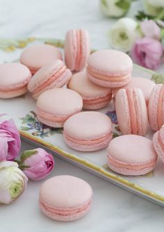 several pink macaroons are on a plate next to flowers and peonies