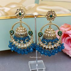 A pair of golden-toned Vaani Jhumka Earrings – Peacock Blue Earrings for Girls with hanging pearls. Size & Other Details Length :  11.5cm Weight : 34gm/pc Material  : Alloy, Pearl, Kundan, Stone work Shape : Dome Shaped Attire :  Lehenga Choli, Salwar Suit, Kurti, Saree, Flared Dress Blue Latkan Danglers For Wedding, Blue Latkans Danglers For Wedding, Blue Festive Jhumkas Drop Earrings, Blue Jhumkas Drop Earrings For Festive Occasions, Blue Bridal Earrings With Latkans, Blue Dangle Earrings For Festivals, Blue Dangle Danglers For Festivals, Blue Chandbali Danglers For Festivals, Festive Blue Chandbali Jhumkas