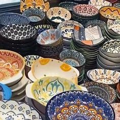 many bowls are stacked on top of each other in different colors and patterns, all with designs