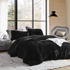 a bed with black comforters and pillows in a room next to a window,