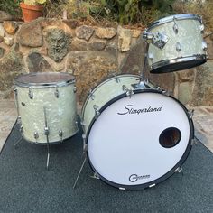 two white drums sitting next to each other on top of a black mat in front of a stone wall