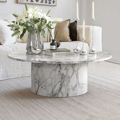 a marble coffee table with vases and flowers on it in front of a couch