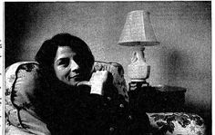 black and white photograph of woman sitting in chair with lamp on table next to her