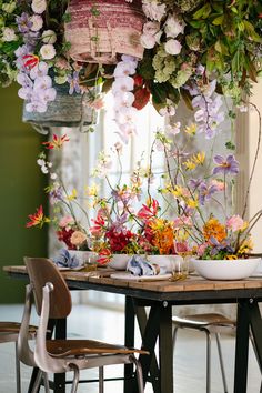 a table topped with lots of flowers next to a hanging basket filled with fruit and veggies