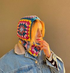 a young woman wearing a crocheted hat and denim jacket with her hand under her chin