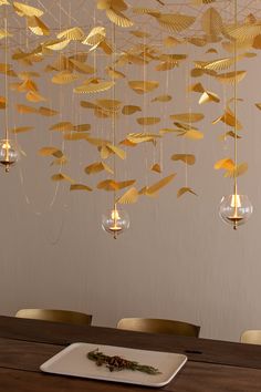 a wooden table topped with a white plate covered in gold leaf chandelier hanging from the ceiling