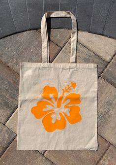 a tote bag with an orange flower on it sitting on a brick walkway next to a wall