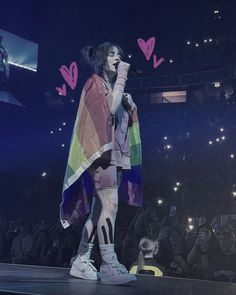 a person standing on top of a stage with a rainbow blanket over their shoulders and hands in the air