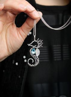 a woman holding onto a silver necklace with a blue stone in the shape of a bird