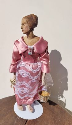 a statue of a woman wearing a pink dress and holding a basket on top of a wooden table