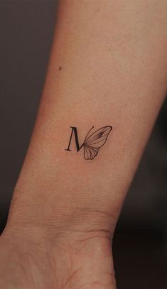 a small butterfly tattoo on the wrist that reads m and is black with a white outline