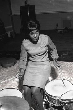 a woman sitting on top of a bed next to two drum sticks in front of her