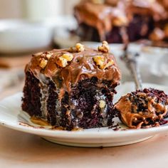 a piece of chocolate cake on a plate with a bite taken out of it and the rest of the cake in the background