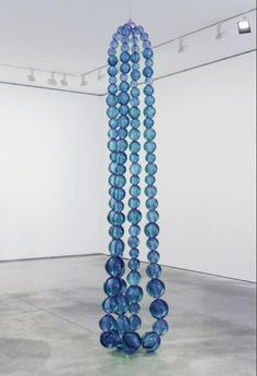 blue glass beads hanging from the ceiling in an empty room with white walls and concrete flooring