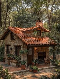 a small stone house in the woods with potted plants on the porch and brick roof