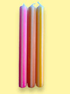 three multicolored candles sitting next to each other on a yellow background with one burning