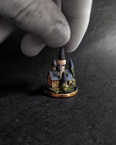 a miniature model of a castle being held up by a person's hand on a black surface