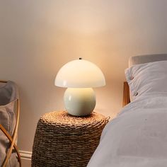 a white lamp sitting on top of a wicker table next to a bed with pillows