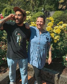 a man and woman standing next to each other in front of yellow flowers on display