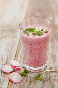 a glass filled with pink smoothie next to sliced radishes on a wooden table