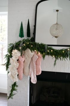 stockings hanging from a mantel decorated with christmas greenery and lights in front of a fireplace