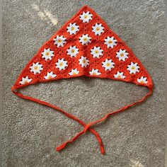 a red and white crocheted hat with daisies on the top, sitting on carpet