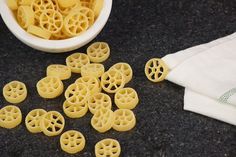 small pieces of yellow pasta next to a bowl of noodles on a black counter top