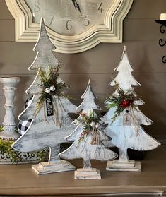 three wooden christmas trees sitting on top of a table next to a clock and candle holder