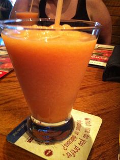 a person sitting at a table with an orange drink in front of them and a card on the table