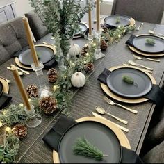 the table is set with black and gold plates, silverware, pine cones, greenery, candlesticks