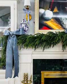 a christmas mantle decorated with pine branches and blue ribbon, next to a fireplace mantel