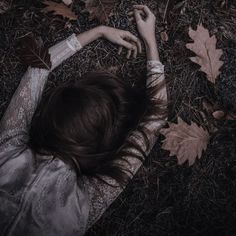 a woman laying in the grass with her hands on her head and leaves around her