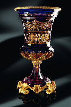 an ornate glass vase sitting on top of a black surface with gold trimmings