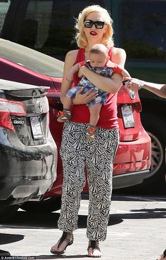 a woman holding a baby in her arms while walking down the street with cars behind her