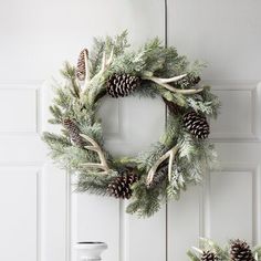 two wreaths with pine cones and antlers hanging from the front door, next to a bottle of wine