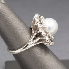 This gorgeous pearl ring looks like it was meant for royalty. The ring features a center round white pearl with silver overtones. The pearl measures 9.5mm and has beautiful luster. The pearl is surrounded by a frame of round single cut diamonds and additional diamonds are tucked into the scalloped edges. The total diamond weight is approximately 0.48cttw and the stones are VS2 to SI1 clarity with G/H color. The effect of the symmetry is mesmerizing. Overall the ring measures 19.83mm in diameter. Silver Diamond Pearl Ring With Halo Setting, Silver Pearl Ring With Diamond Accents For Wedding, Heirloom Silver Pearl Ring With Diamond Accents, Diamond Cocktail Ring, Vintage Pearl, Diamond Cocktail Rings, Vintage Pearls, Scalloped Edges, Cocktail Ring