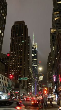 a city street filled with traffic and tall buildings at night, in the distance are skyscrapers